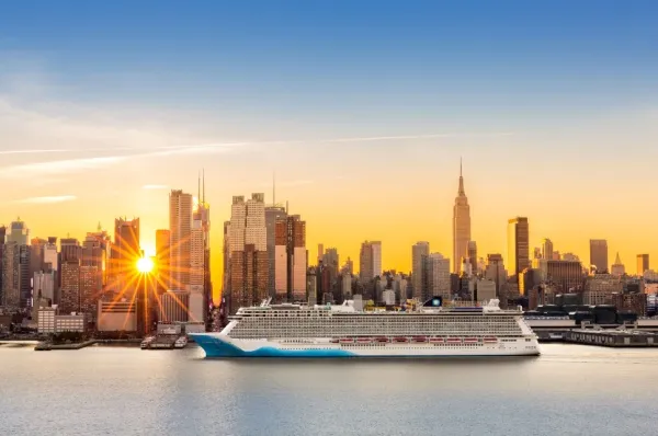 Ein großes Kreuzfahrtschiff fährt entlang der New Yorker Skyline bei Sonnenuntergang.