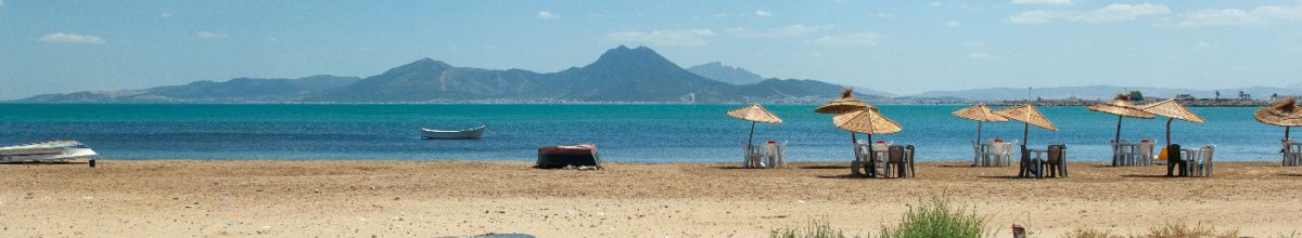 Der Strand von La Goulette angrenzend an das Meer mit einer Bergkette im Hintergrund bei Tag.