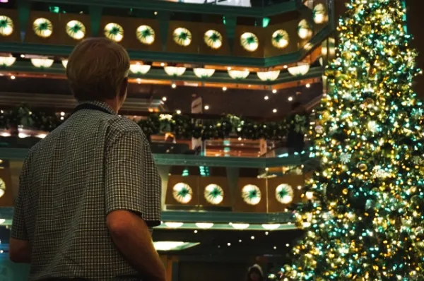 Entspannt Weihnachten feiern Ein Mann schaut auf einen beleuchteten Weihnachtsbaum im Festsaal eines Kreuzfahrtschiffs.