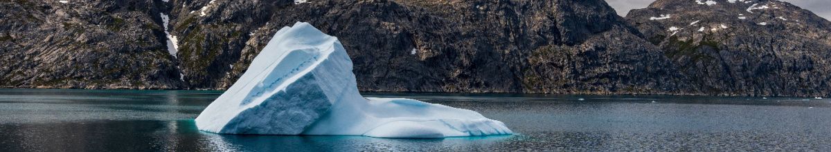 Ein Eisberg im Prins Christian Sund bei Tag mit Felsen im Hintergrund.