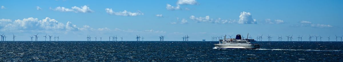 Totale vom Meer bei Bornholm mit einem Schiff und vielen Windkraftturbinen im Hintergrund.