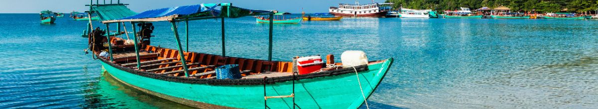 EIn Ruderboot auf kristallklarem Wasser am Strand mit den Tropen im Hintergrund.