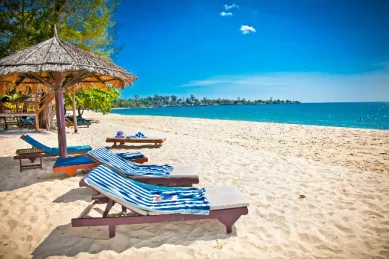 Ein Strand mit Liegen und Palmen angrenzend an ein azurblaues Meer bei praller Sonne.