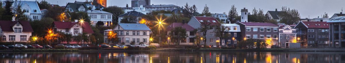 DIe Hafengrenze der Stadt Seyðisfjörður reflektierend im abendlichen Wasser mit warmen Lichtern.