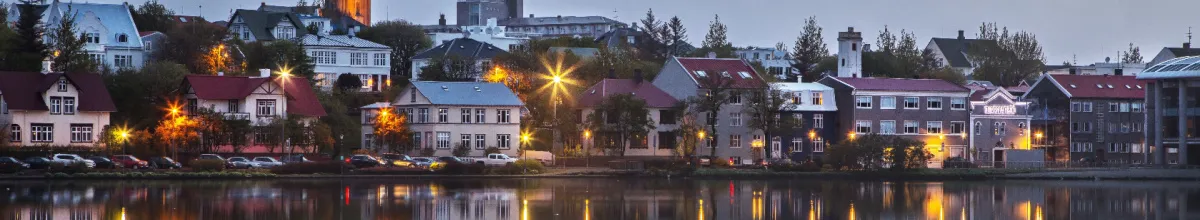 DIe Hafengrenze der Stadt Seyðisfjörður reflektierend im abendlichen Wasser mit warmen Lichtern.