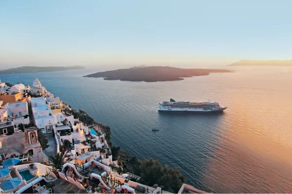 Die Norwegian Jade fährt entlang der griechischen Küste vor Santorini in einen Sonnenuntergang.