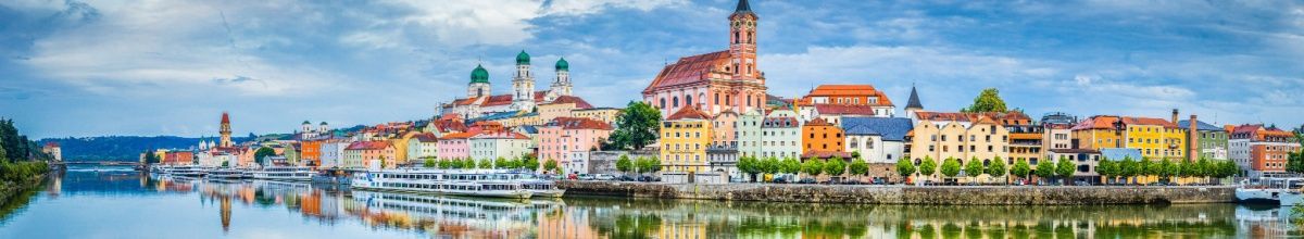 Passau an der Donau mit bunten Häusern, Flusskreuzfahrtschiff und Kirchturm.