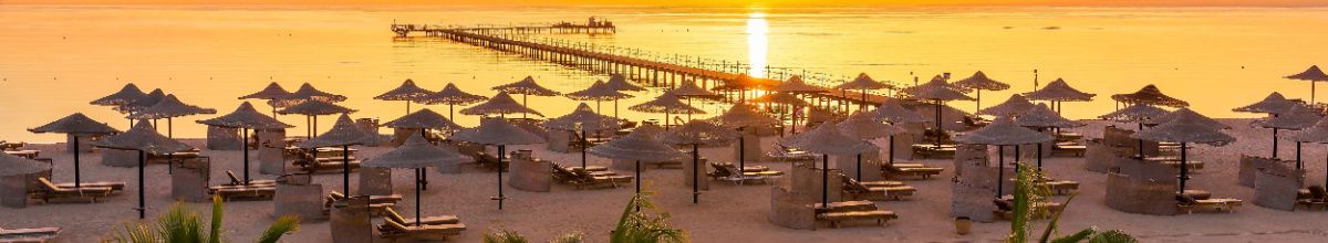 Eine Strandpromenade mit einer Vielzahl an Strandschirmen gebadet im goldenen Licht der Abendsonne Ägyptens.