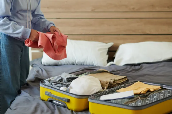 Ein Mann der Kleidung in seinen Koffer packt, welcher auf einem Bett liegt.