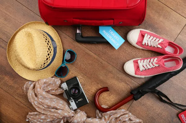 Ungepacktes Reisegepäck bestehend aus Hut, Brille, Schuhen, Kamera und Schal neben einem Koffer.