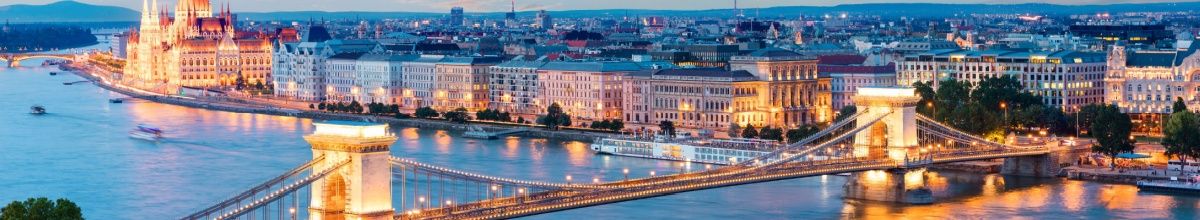 Totale der Hafenkante von Budapest bei Nacht, warm beleuchtet mit einer Brücke.