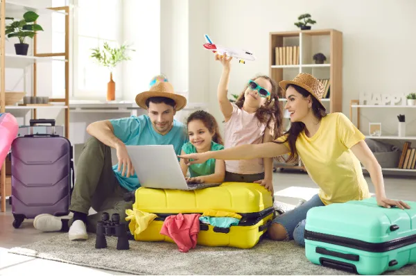 Eine Familie plant eine Kreuzfahrt am Laptop Glückliche Familie mit zwei Kindern sitzt zwischen Koffern auf dem Boden und plant am Laptop ihre Kreuzfahrt.