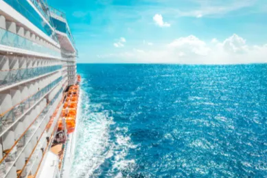 Seitliche Ansicht eines großen Kreuzfahrtschiffes, das bei sonnigem Wetter durch das blaue Meer fährt und eine Heckwelle erzeugt – Sinnbild für eine Kreuzfahrt, die man durch Stornokabinen günstiger finden kann.