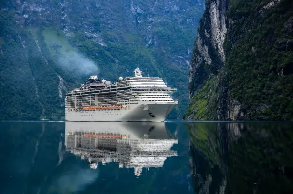 EIn Kreuzfahrtschiff in einem Fjord auf kristallklarem Wasser bei Tag umgeben von Bergen.