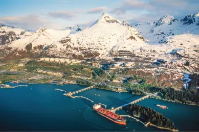 Ein angedocktes Kreuzfahrtschiff an einem Hafen, im Hintergrund ragen schneebedeckte Berge in den Himmel.