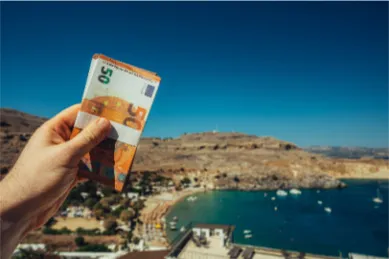 Hand hält Euro-Geldscheine vor einer malerischen Bucht, als Symbol für die Nutzung von Bordguthaben für Landausflüge.