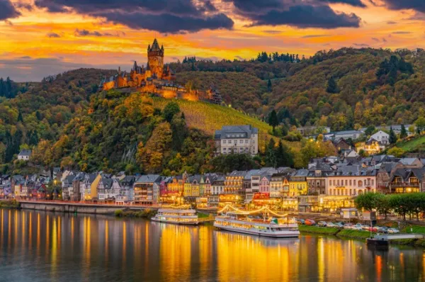 Beleuchtete Reichsburg Cochem bei Sonnenuntergang über der Mosel, Blick auf die Altstadt mit Moselpromenade während einer AMADEUS Flusskreuzfahrt.