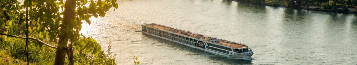 Kreuzfahrtschiff von AMADEUS fährt bei Sonnenschein über einen Fluss.
