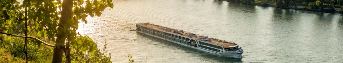 Kreuzfahrtschiff von AMADEUS fährt bei Sonnenschein über einen Fluss.
