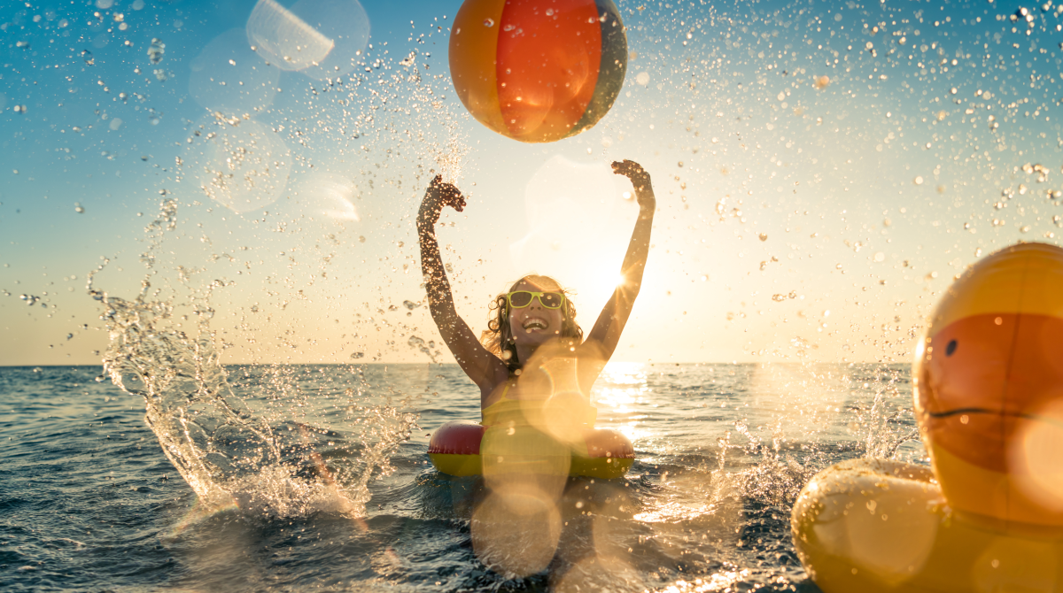Ein glückliches Kind in einem Schwimmring spielt im Meer mit einem Ball.