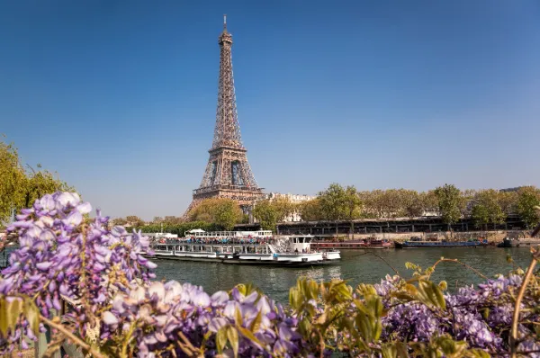 Flusskreuzfahrtschiff auf der Seine in Paris mit dem Eiffelturm und blühenden Blumen im Hintergrund, Symbol für eine Pfingstkreuzfahrt und das Genießen erster Sommergefühle.