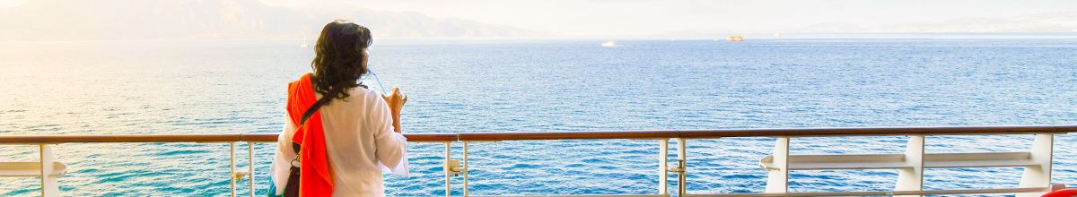 Eine Frau, die alleine an Deck steht und den Sonnenuntergang auf dem Meer betrachtet.