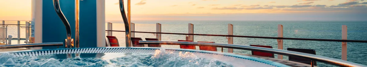 Sprudelnder Whirlpool auf dem Außendeck eines AIDA Kreuzfahrtschiffs bei Sonnenuntergang mit Blick auf das weite Meer und leeren Sonnenliegen.