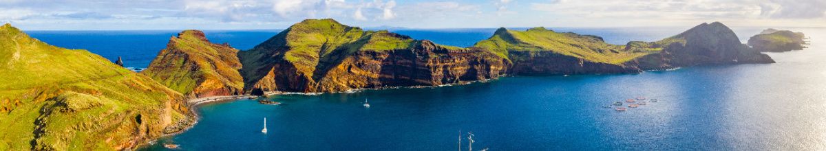 Ein Auschnitt der Küste bei Funchal auf Madeira bei Sonnenschein mit tiefblauem Wasser und grünen Hügeln.