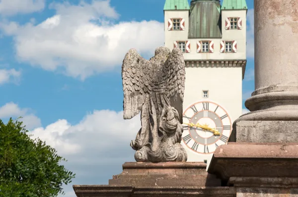 Eine alte Engelsstatue von hinten und im Hintergrund ein alter Glockenturm.