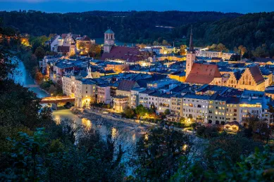 Straubing bei Nacht mit beleuchteten Fenstern und der Donau, die an der Stadt entlang fließt.
