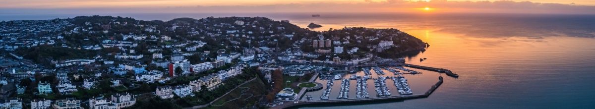 Panoramablick auf die Stadt Torquay, während im Hintergrund die Sonne über dem Meer untergeht.