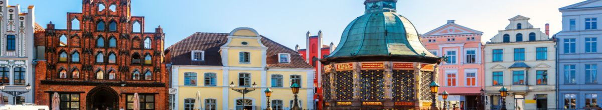Die Altstadt der Hansestadt Wismar bei Tag, gespickt mit bunten Gebäuden und einem Pavillion.