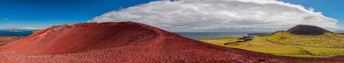 Ausblick über die Hügel Heimaeys bei Tag, mit einem rot-bewachsenen Hügel im Vordergrund.