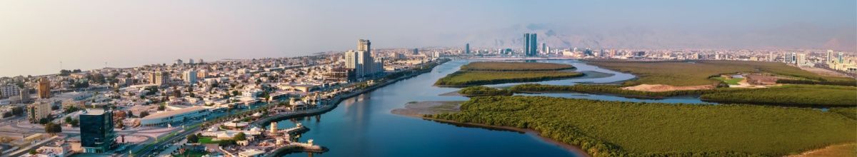Stadtpanorama von Ra's al-Chaimah mit Hochhäusern, Wasserwegen und einer großen Grünanlage.