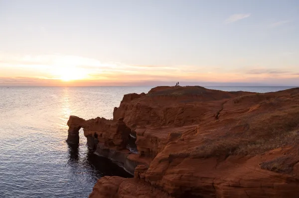 Klippen auf Cap-aux-Meules Ein Vista der roten, zerklüfteten Sandsteinklippen auf Cap-aux-Meules bei Sonnenuntergang mit dem ruhigen Meer im Hintergrund.