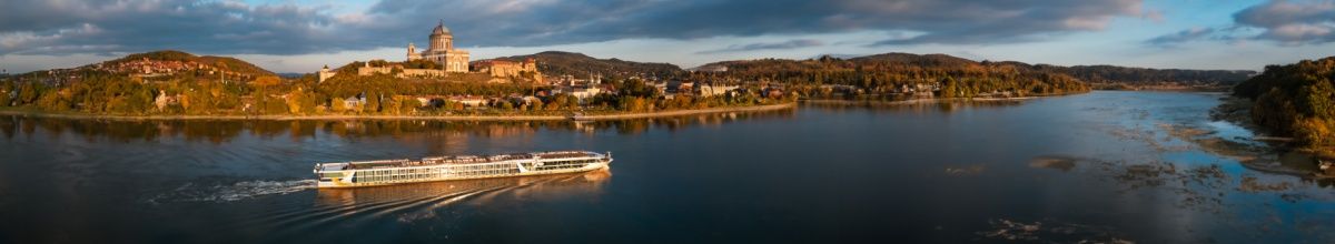 MS VistaSky fährt auf einem Fluss entlang eines sonnenbeschienenen Ufers.