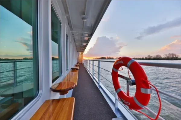 1AVista Flusskreuzfahrten Die Seitenansicht eines Schiffes auf einem Fluss mit Bänken und einem Rettungsring.