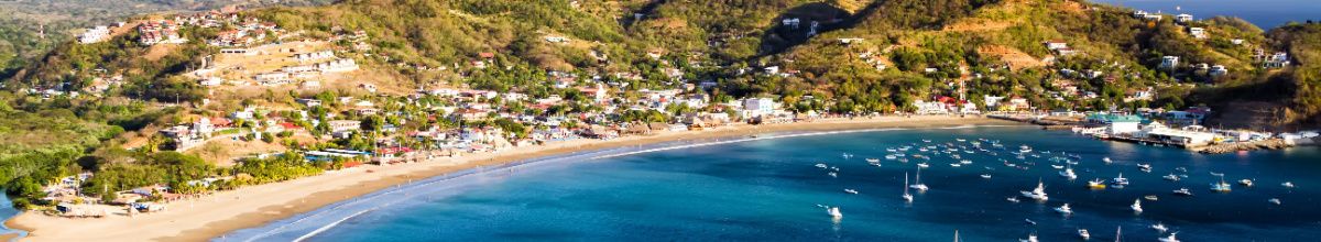 Totale des Strands bei San Juan del Sur mit azurblauem Wasser, Booten und der angrenzenden Stadt.