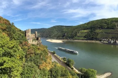Ein Schiff der 1AVista-Flotte fährt über einem Fluss, auf einem Hügel im Vordergrund thront eine Ruine.