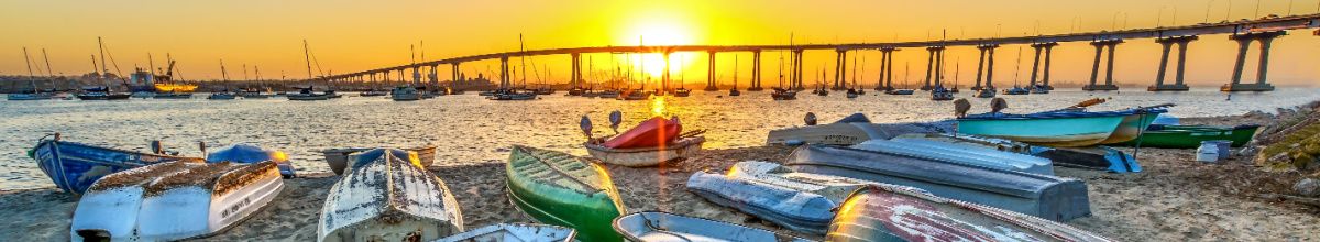 Ein Strand mit Ruderbooten bei Sonnenuntergang und im Hintergrund die Coronado-Brücke.