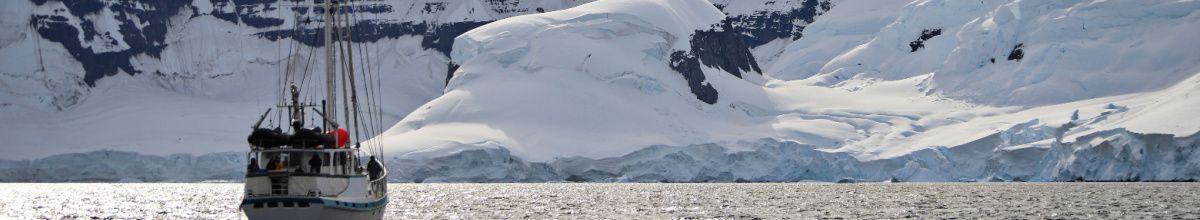 Ein Schiff an der Antarktisküste vor Port Lockroy bei Tag mit einer Schneelandschaft im Hintergrund.