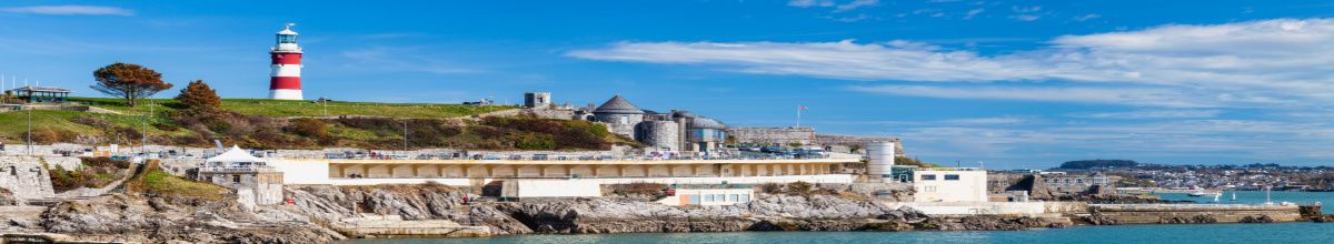 Ein rot-weiß getünchter Leuchtturm an der Küste von Plymouth bei Tag.