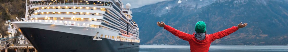 Ein Kreuzfartschiff mit einer Frau die dem Schiff entgegenwinkt vor der Küste von Ketchikan bei Tag.