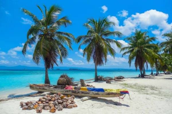Ein Strand auf den San-Blas-Inseln mit Palmen und einem kleinen Boot an Land, bei Sonnenschein.