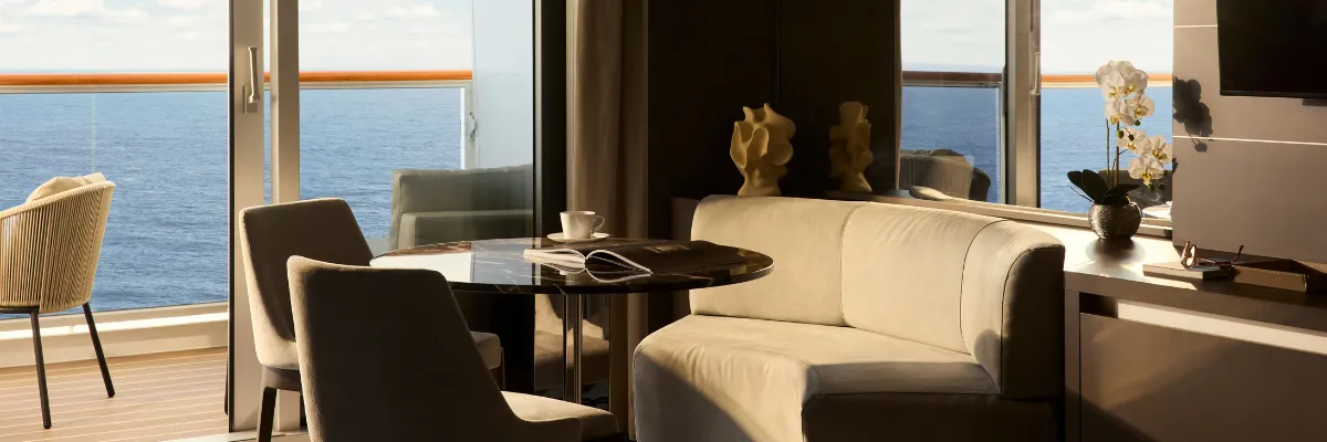 Deluxe Penthouse Die Wohnecke mit Sitzbank und Tisch neben den Panoramafenstern zum Balkon in einer Deluxe Penthouse Suite an Bord der EXPLORA II