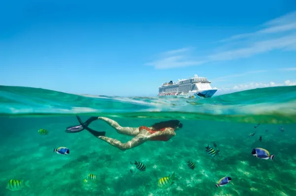 Karibikkreuzfahrt mit NCL Ein Schiff der Norwegian Cruise Line fährt über das türkisfarbene Wasser der Karibik, im Vordergrund schnorchelt eine Frau mit bunten Fischen.