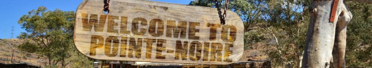 Ein Holzschild auf dem Pointe-Noire steht bei Tag mit dem Busch im Hintergrund.