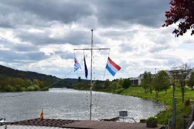 Ein Ausblick über die Mosel von einem Pier aus, auf dem die luxemburgische und europäische Flagge gehisst sind.