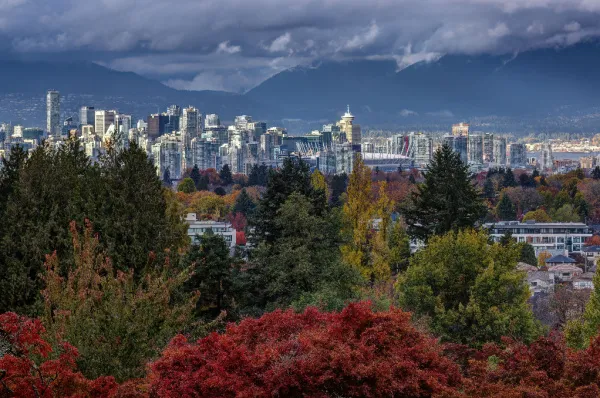 Die Skyline von Vancouver mit bunten Bäumen im Vordergrund und einem Gebirge im Hintergrund bei Tag.