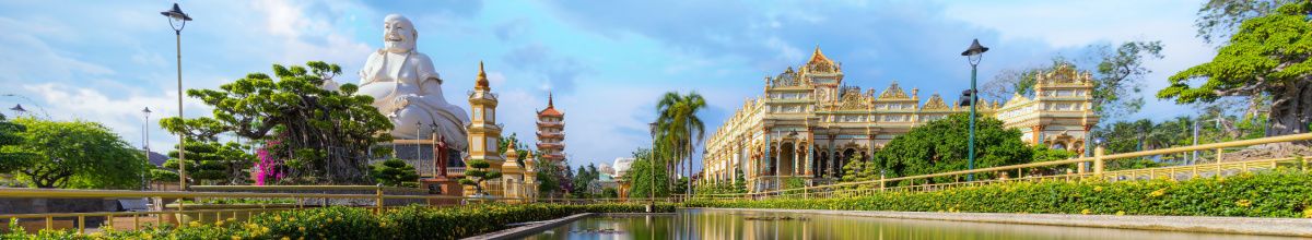 Die Tempellandschaft der Vinh Trang Pagode bei Tag mit einem reich verziertem Tempel und einer großen Buddha Statue.